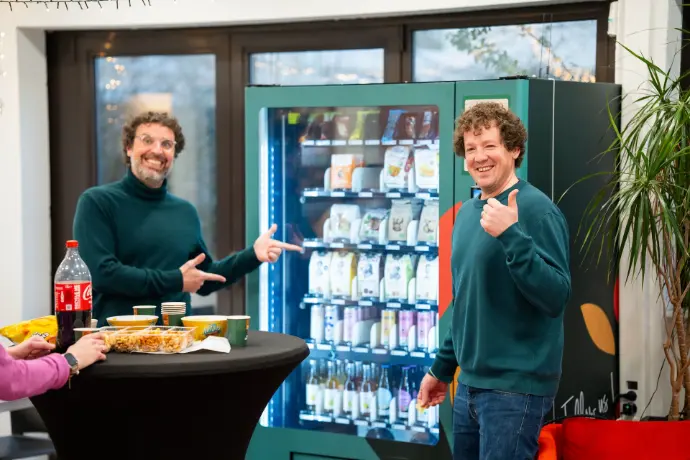 Un homme avec son pouce vers le haut, sourire au lèvre et un autre montrant vers celui-ci sourire au lève entouré de snack et de boissons lors d'un évènement de networking professionnel